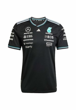 Personne portant un t-shirt noir de l'équipe Mercedes AMG Petronas de Formule 1 avec les logos des sponsors, un jean noir et des baskets noires avec des bandes turquoise.