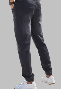 Pantalones jogger de mezclilla oscura con puños elásticos y bolsillos, combinados con zapatillas blancas. La tela tiene una textura suave y un ligero desvanecimiento.