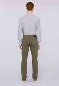 Pantalones verde oliva con un diseño ajustado, que cuentan con dos bolsillos traseros y una etiqueta visible en la cintura. El modelo lleva una camiseta gris claro.