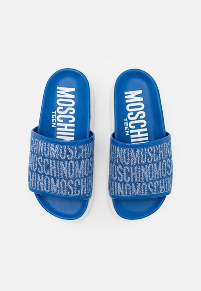 Blå sandaler med en teksturert rem som har gjentagende hvite bokstaver. Myk innside og flat hvit såle. Merkenavn trykket på fotbeddet.