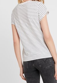 Camisa de manga corta a rayas en gris claro con rayas horizontales negras. Tela suave, corte relajado, escote redondeado, diseño básico.