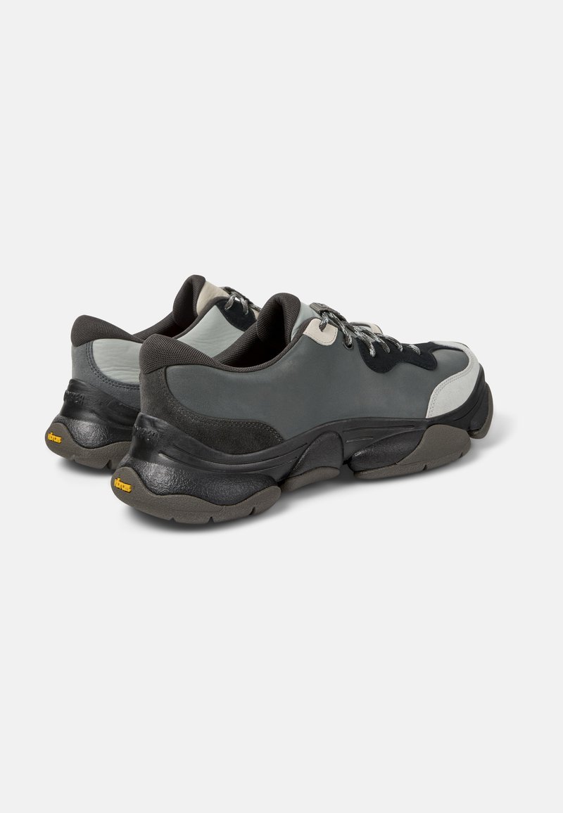 Graue und schwarze Sneakers mit einer klobigen Sohle, Obermaterial aus Wildleder und synthetischem Material, kontrastierende Texturen und Schnürdesign. Vibram-Logo auf der Sohle.
