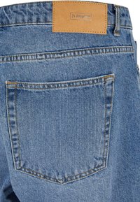 Jeans en denim de couleur bleu clair, tissu texturé, patch en cuir étiqueté "2Y PREMIUM" et une seule poche arrière avec des détails de couture.