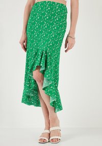 Žalia gėlių sijonas su raukšlėta hemline, turintis aptemptą viršutinę dalį ir plačią apatinę dalį. Pagamintas iš lengvos medžiagos su mažomis baltomis gėlėmis.