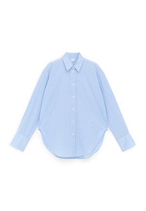 Chemise bleu clair à manches longues avec petit motif à carreaux, col pointu et ourlet arrondi, posée à plat sur fond blanc.