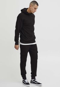 Zwarte zip-up hoodie met een voorzak, gecombineerd met bijpassende cargobroek met zijkzakken en elastische manchetten, gedragen met zwarte sneakers.