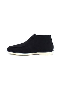 Bottines en suède noir avec un design lisse et courbé, semelle en caoutchouc blanche, et un style minimaliste sans matériel ou accents visibles.