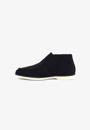 Bottines en suède noir avec un design lisse et courbé, semelle en caoutchouc blanche, et un style minimaliste sans matériel ou accents visibles.