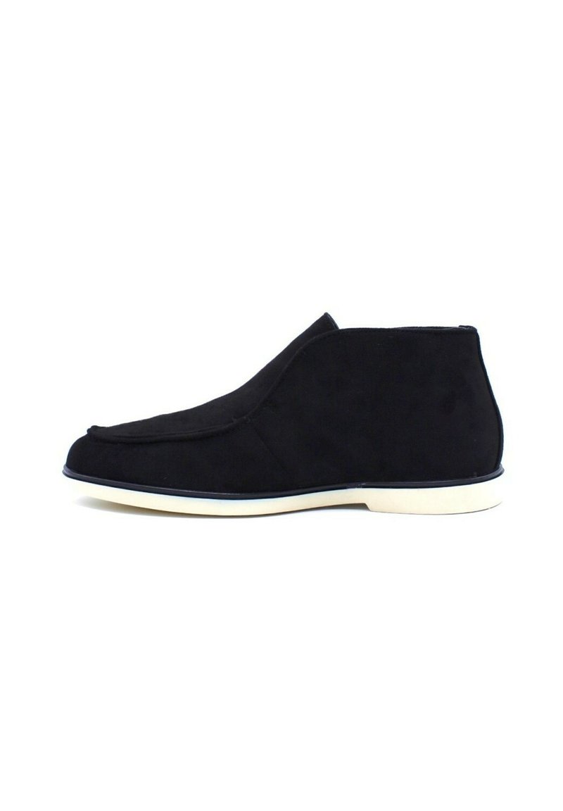 Bottines en suède noir avec un design lisse et courbé, semelle en caoutchouc blanche, et un style minimaliste sans matériel ou accents visibles.