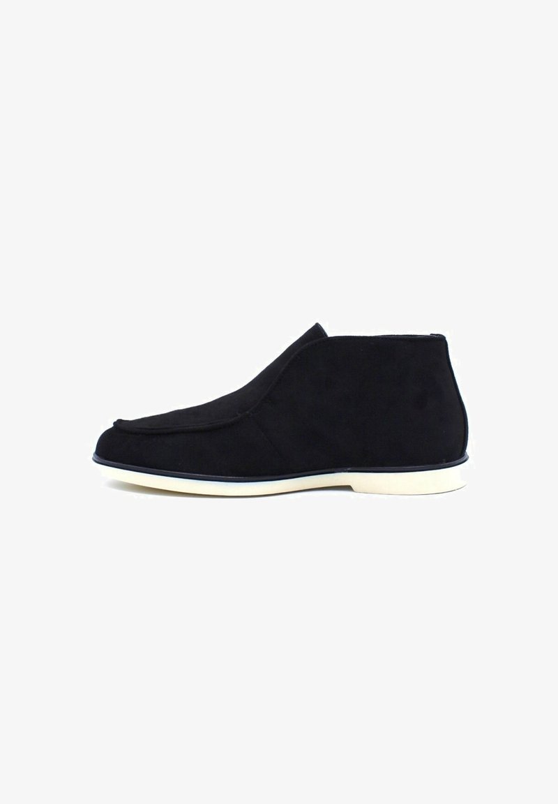 Bottines en suède noir avec un design lisse et courbé, semelle en caoutchouc blanche, et un style minimaliste sans matériel ou accents visibles.