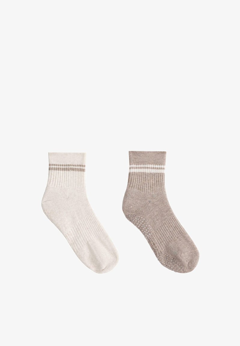 Paire de chaussettes à la cheville, une crème avec deux rayures beige, une marron clair avec deux rayures blanches et des grips antidérapants sous la semelle.