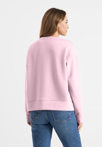 Roze sweatshirt met een ontspannen pasvorm, ronde hals en geribbelde manchetten, gecombineerd met blauwe denim jeans. Zachte textuur, minimalistisch ontwerp.
