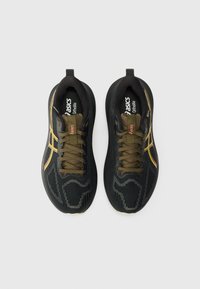 Chaussures de sport noires avec une tige texturée, lacets vert olive et accents dorés. Présente un design moderne et une semelle rembourrée.