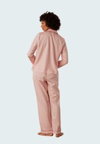 Randig pyjamasätt bestående av en skjorta med krage och matchande byxor i rosa och vitt med röda accentfärger, tillverkat av lättviktig tyg.