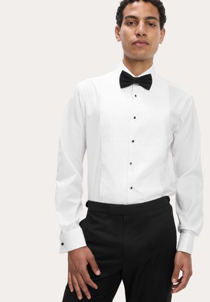 Hvid skjorte med sort butterfly. Har plisseret front, sorte knapper og franske manchetter med sorte detaljer. Bæres med sorte bukser.