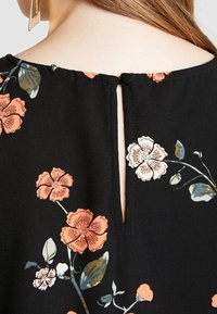 Detailní záběr na krk a horní část zad v černých květovaných šatech s oranžovými a bílými květy a výstřihem ve tvaru klíčové dírky.