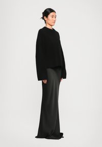 Maglione corto nero e pelo con maniche lunghe abbinato a una gonna in satin nero di lunghezza maxi, creando una silhouette liscia e slanciata.