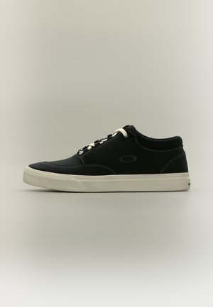 Schwarzer Low-Top-Sneaker mit weißer Sohle und Schnürsenkeln, mit subtiler Nahtangabe und kleinem ovalem Logo an der Seite, auf neutralem Hintergrund.
