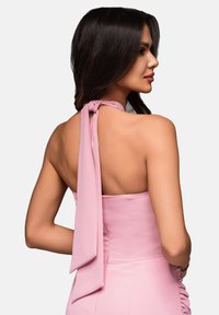 Růžové halter šaty s mašlí detail na krku, hladká textilie a přiléhavý střih, s řaseným materiálem po straně.