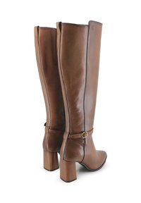 Botas de cuero marrón hasta la rodilla con tacón cuadrado, que cuentan con una correa decorativa en el tobillo y un sutil detalle de costura. Textura suave en toda la superficie.