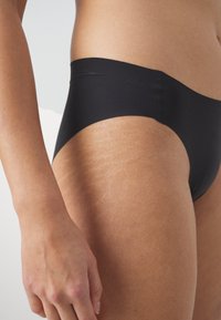 Zwarte bikini broek gemaakt van een gladde stof, met een middenhoogte snit en een minimalistisch ontwerp. Bevat zachte randen en geen zichtbare hardware.