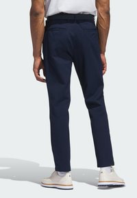 Marineblauwe broek van gladde stof, met een slim fit, twee achterzakken en gecombineerd met lichtgekleurde schoenen.