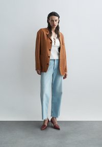 Brun suedet blazer med knappestolpe, hvit ribbet topp med blonderdetaljer, lyseblå vide jeans og røde spisse hæler.