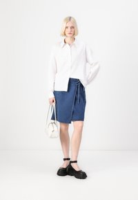 Hvit skjorte med broderte detaljer, kombinert med et denimbåndskjørt. Svarte kraftige sko og en liten hvit håndveske fullfører antrekket.