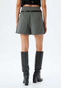 Pantalones cortos grises de corte recto, con bolsillos laterales y una cinturilla negra mate. Combinados con botas de cuero negras hasta la rodilla.