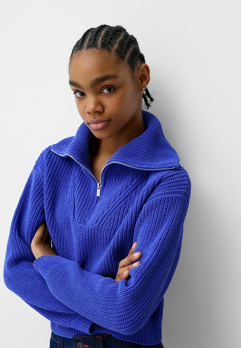Maglione lavorato a maglia di un vivace blu royal, con collo alto, chiusura con mezza zip e coste testurizzate. Design aderente con maniche lunghe.