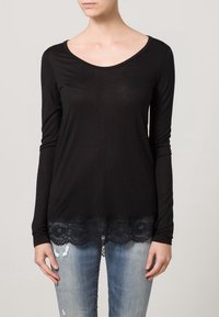 Top negro de manga larga hecho de tela ligera, con un borde de encaje en el dobladillo, combinado con jeans de mezclilla claros y desgastados.