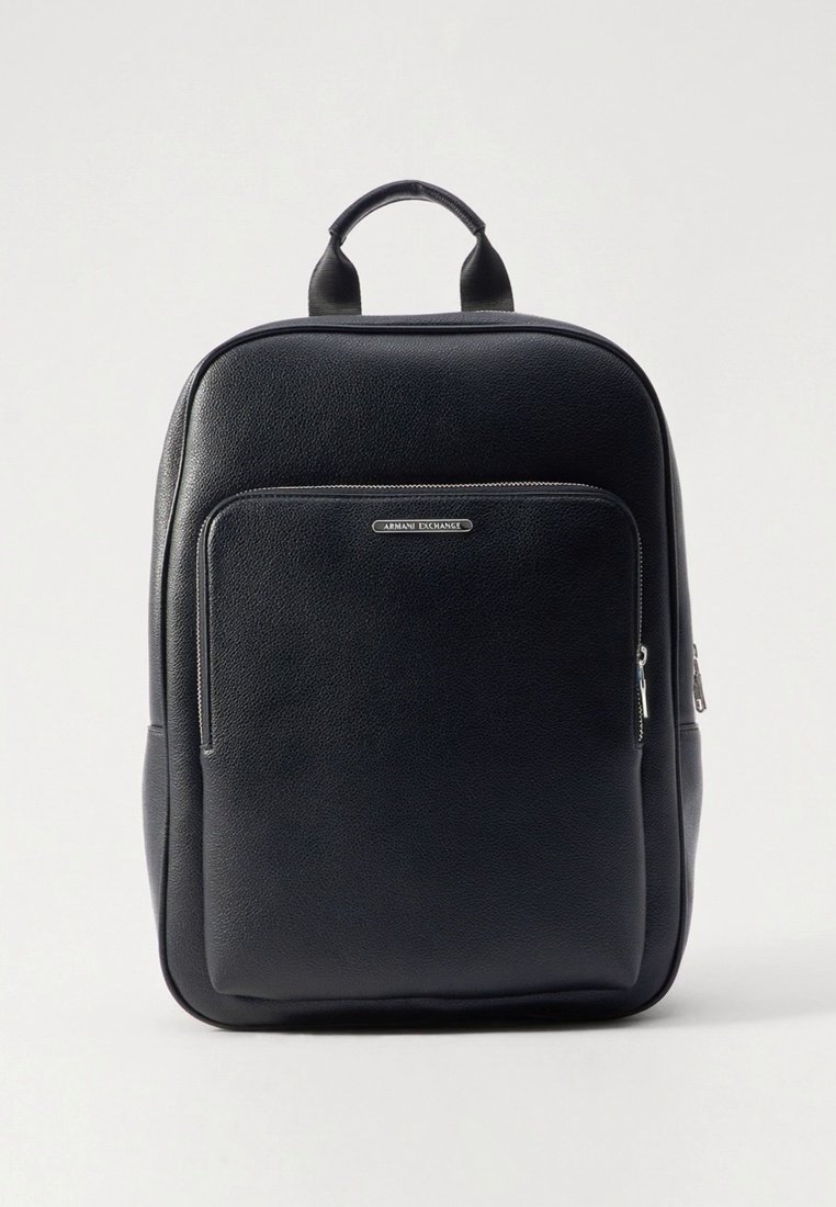 Sac à dos en cuir noir à texture lisse, avec un compartiment central zippé, une poche avant et une poignée supérieure. Doté de ferrures métalliques de marque.