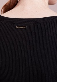 Svart ribbad tröja med breda axlar, utrustad med en metallbeslagsetikett på baksidan med "Michael Kors" ingraverat.