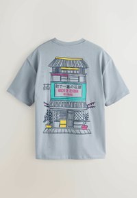 Hellblaues T-Shirt mit einer bunten Illustration eines traditionellen japanischen zweistöckigen Gebäudes und japanischem sowie englischem Text auf der Rückseite.