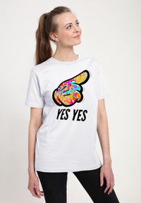 Hvid T-shirt med et farverigt grafisk design af en pegende hånd og teksten "JA JA" i fede sorte bogstaver.