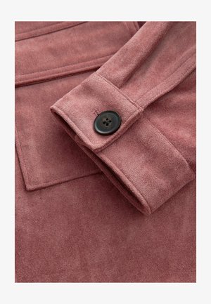 Manga de chaqueta de ante rosa con un detalle de botón negro. Presenta una textura lisa y costuras limpias, destacando la suavidad de la tela.