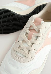Baskets avec une tige synthétique blanche, des accents rose clair, un design à lacets et une semelle en caoutchouc noir texturé. Détails en daim sur les côtés.
