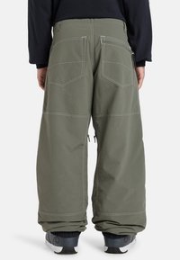 Green wide-legged trousers with white stitching, featuring two back pockets and ankle zippers, made of a lightweight fabric.