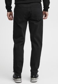 Black denim jeans with a straight fit, featuring two back pockets and a smooth texture; paired with black and gray athletic shoes.