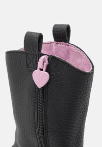 Stivale in ecopelle nera con superficie testurizzata, fodera interna rosa e una zip a forma di cuore rosa. Presenta due linguette per aiutare a indossarlo.