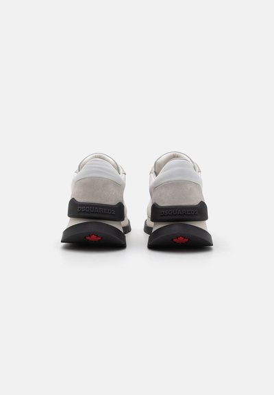 Baskets grises et blanches avec un dessus texturé, un support de talon noir et un détail de feuille d'érable rouge sur la semelle. Design minimaliste avec des lignes épurées.