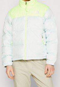 Jasnoniebieska ocieplana kurtka puchowa z wysokim kołnierzem, neonowozielonymi akcentami i zapięciem z przodu; posiada boczne kieszenie i luźny krój.