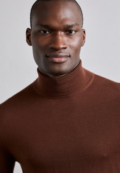 Rjav rebrast turtleneck pulover, izdelan iz gladkega pletenega materiala. Ima visok ovratnik in oprijet silhueto, ki poudarja predel vratu.