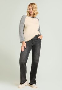 Jasnobeżowy sweter z szarymi rękawami, proste ciemnoszare dżinsy oraz kremowe trampki. Miękka tekstura, luźny krój i casualowy design.