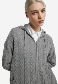 Szara bluza z kapturem o splocie warkoczowym, z pełnym suwakiem, oversize'owym krojem i dwoma przednimi kieszeniami. Posiada luźny kaptur i teksturowaną tkaninę.