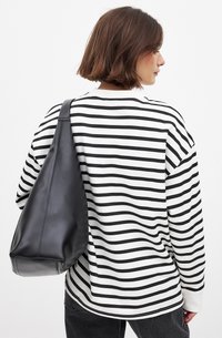 Chemise à manches longues rayée noir et blanc portée avec un sac à épaule en cuir noir doux ; texture lisse, coupe décontractée, détails de couture visibles.