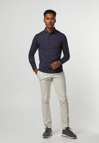 Marineblaue Langarm-Polohemd mit Dreiknopf-Leiste, kombiniert mit hellbeigen Hosen und grauen Sneakers mit kontrastierenden Schnürsenkeln.