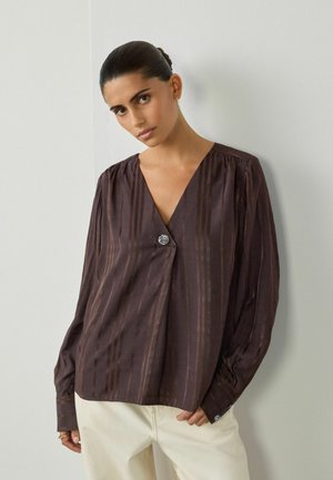 Blusa a righe marroni con scollatura a V profonda e un bottone decorativo davanti. Presenta maniche lunghe e un materiale leggero.