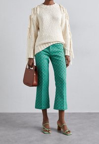 Tjock krämfärgad stickad tröja med fransdetaljer, kombinerad med gröna mönstrade kvartslånga byxor. En brun handväska och gröna sandaletter med remmar fulländar looken.