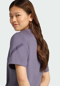 Lila kortärmad skjorta med rundad halsringning, som har en slank design och en kontrasterande accent på vänster ärm. Slät tygstruktur.